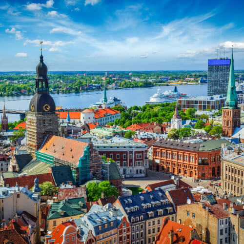 Riga, Latvia city skyline featuring historic Old Town rooftops, church towers, and the Daugava River under a blue sky, showcasing the city’s urban landscape.